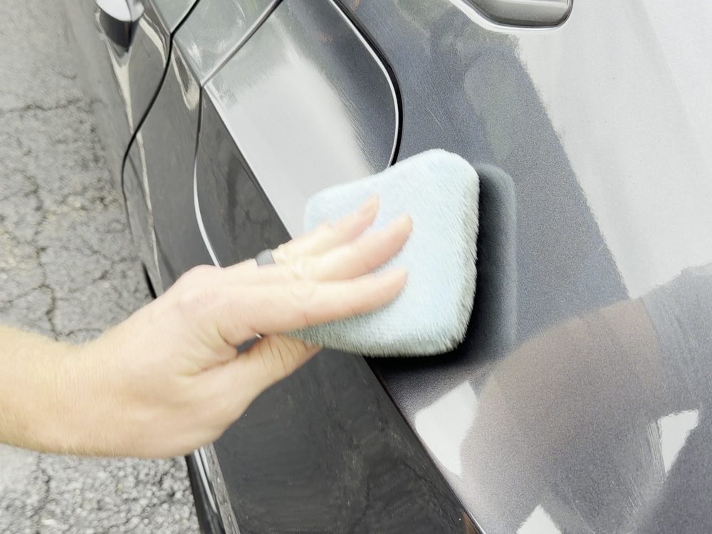 Ceramic coating being wiped onto a grey car's rear quarter with an applicator block