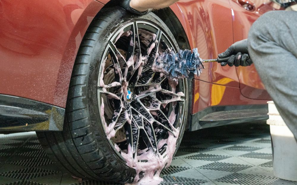 A technician brushing iron remover through a BMW wheel, the product turning purple