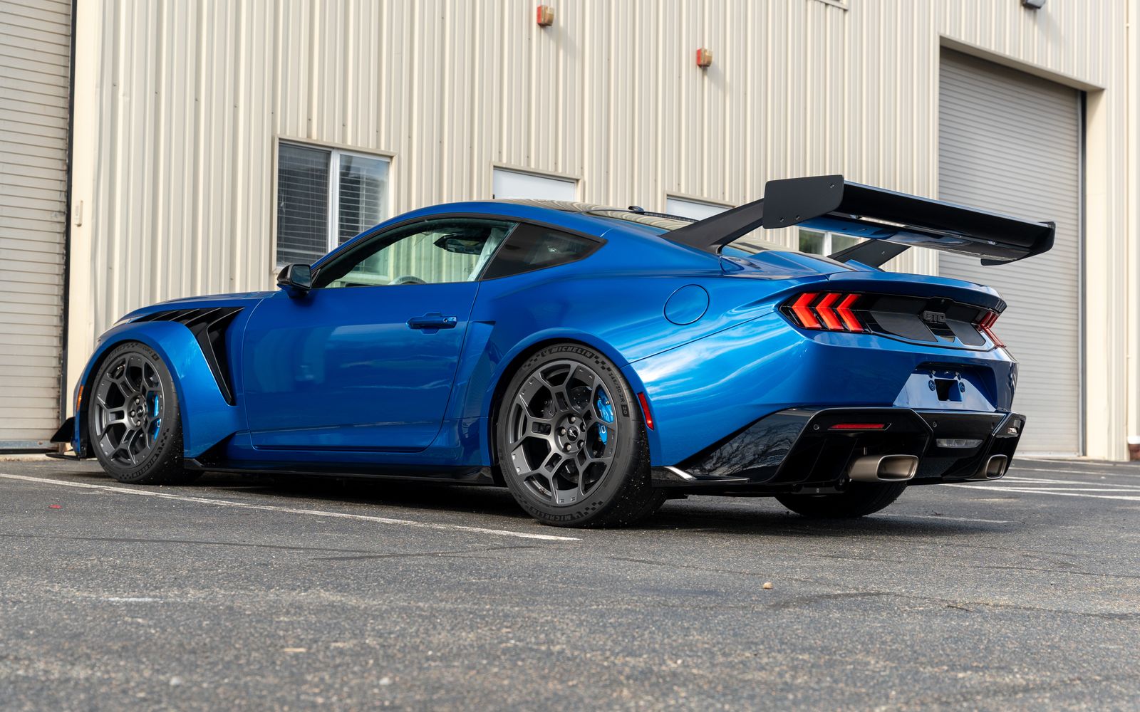 A blue Ford Mustang GTD from the rear three quarter, its paint reflecting the building beside it
