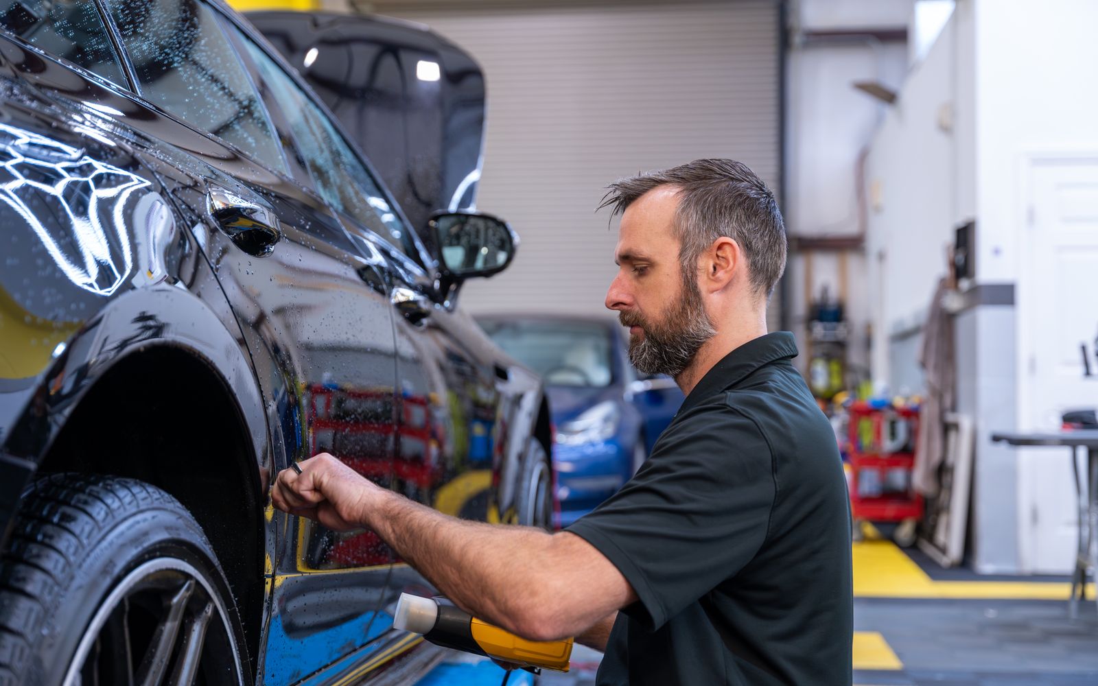 An ACP technician heat-shaping paint protection film on the door of a black car