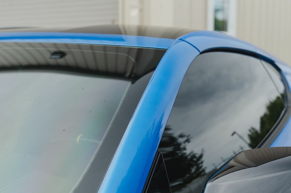 Close up of a blue Corvette's dark tinted side glass reflecting the sky