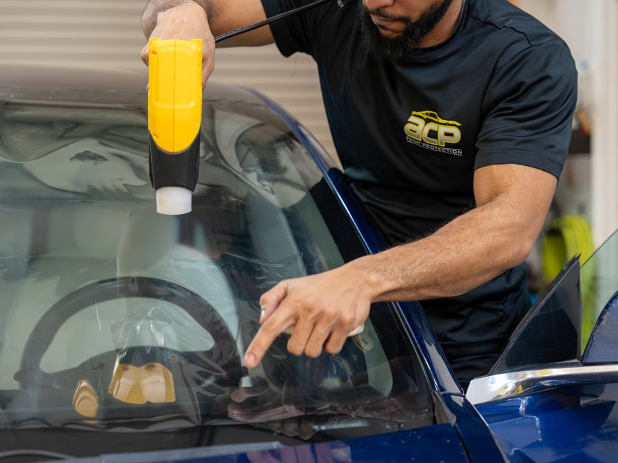 An ACP technician heat-shaping film on a windshield